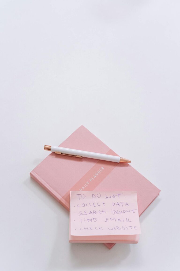 Flat lay of pink planner, pen, and sticky notes on white background.